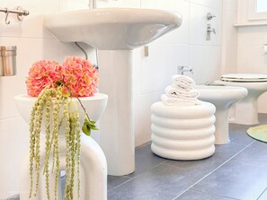 A bathroom with a white sink, toilet, and bidet. There are pink flowers on the sink and a white towel stack. - Flatsharing - Gioia Red Retreat – 3 Bedrooms (Milan)