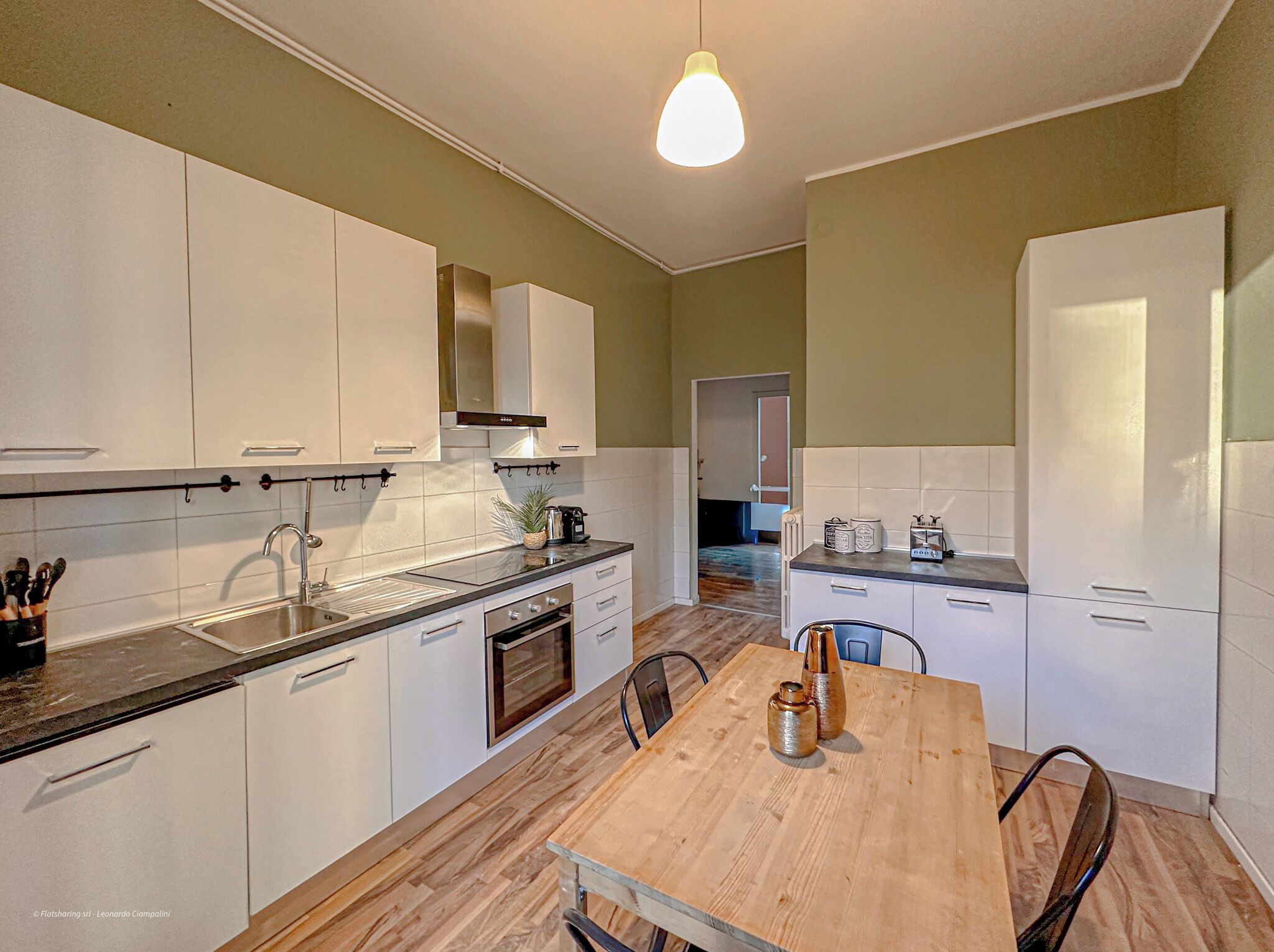 Una cocina moderna con armarios blancos, una mesa de comedor de madera y una lámpara colgante.