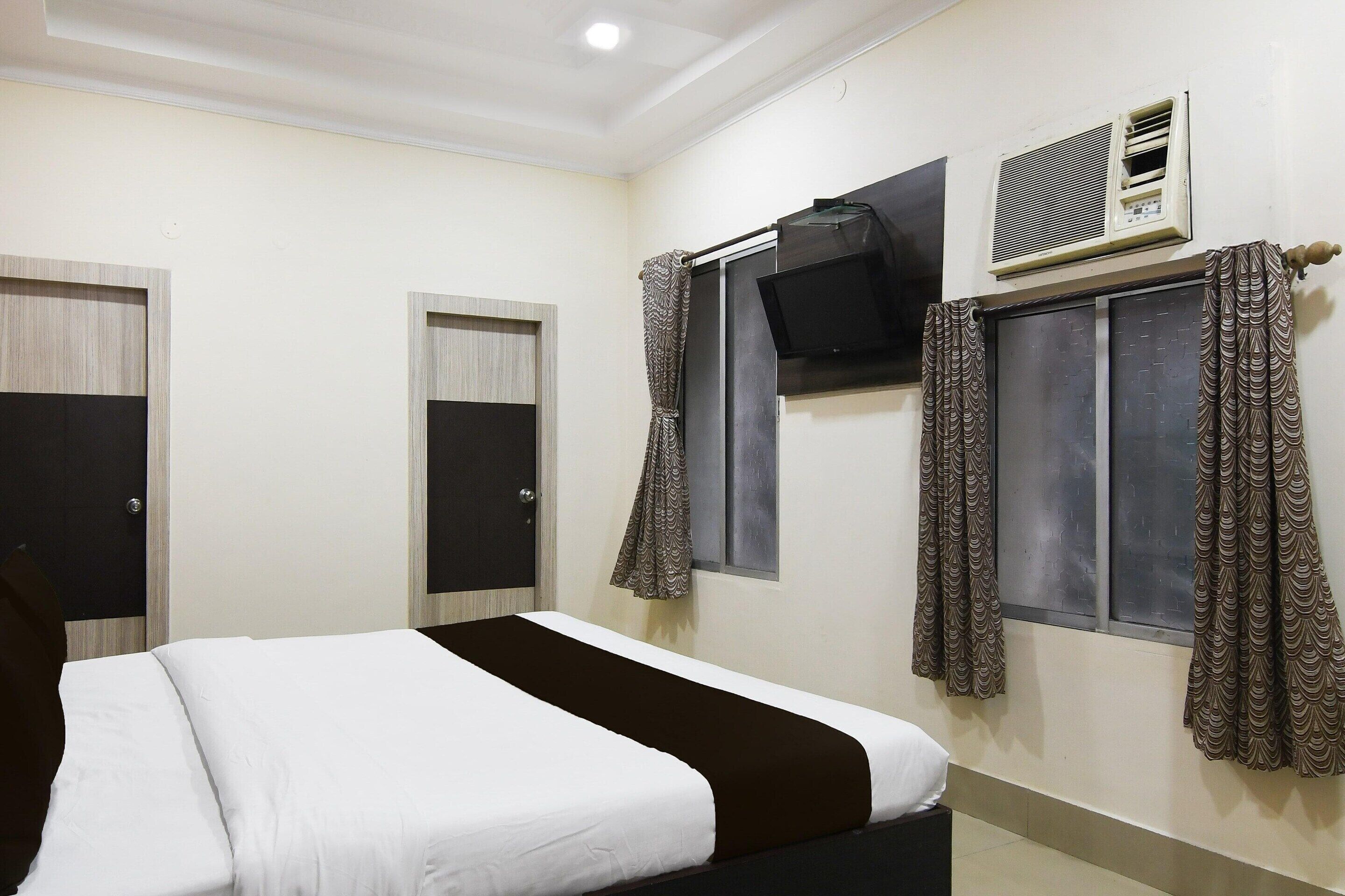 A hotel room with a bed, a wardrobe, a television, and an air conditioning unit.