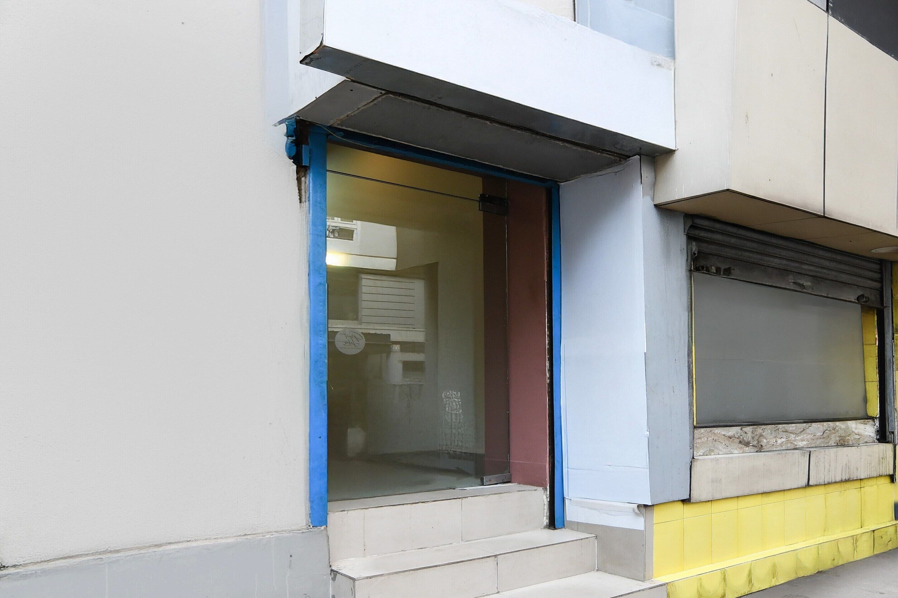 A building with a glass door entrance, a set of steps leading up to it, and a closed shutter to the right.