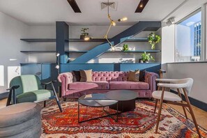 Ein modernes Wohnzimmer mit einem rosafarbenen Sofa, einem runden Couchtisch und einer blauen Treppe.
