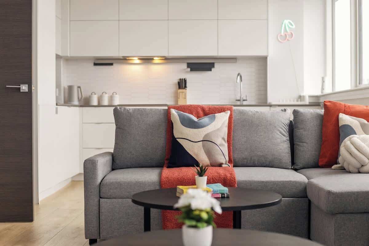A modern living room with a grey sofa, a round coffee table, and a kitchen in the background.