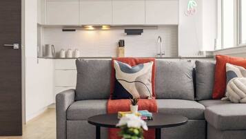 A modern living room with a grey sofa, a round coffee table, and a kitchen in the background.