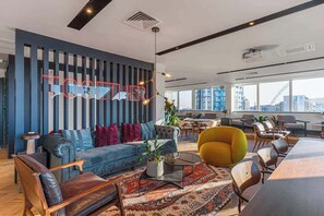 Ein moderner Arbeitsraum mit einer blauen und weißen Streifenwand, einem großen Sofa, einem gelben Sessel und einem Esstisch.