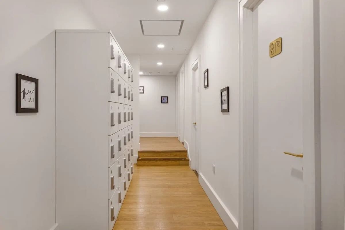 A hallway with a wooden floor, white walls, and a series of lockers on one side.
