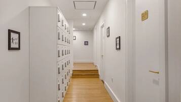 A hallway with a wooden floor, white walls, and a series of lockers on one side.