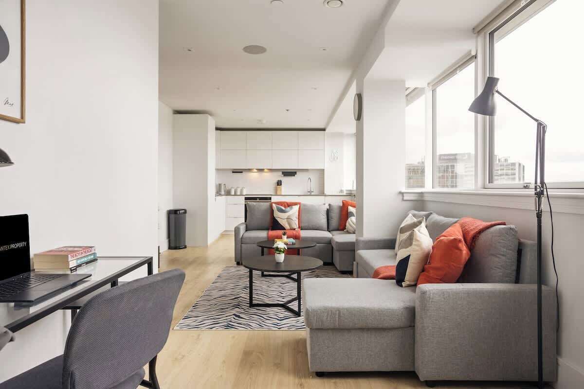 A modern living room with a grey sofa, a coffee table, and a laptop on a desk.