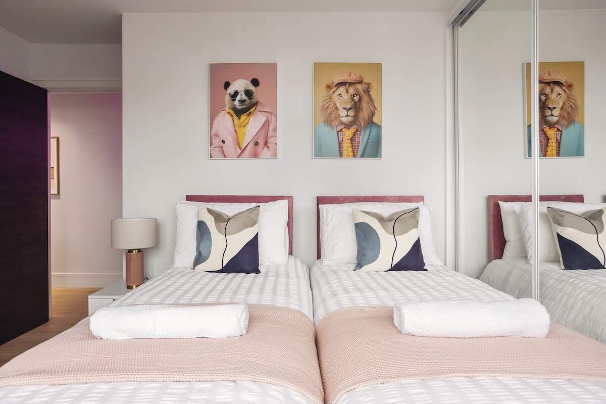 A hotel room with two beds, a mirror, and artwork on the wall.
