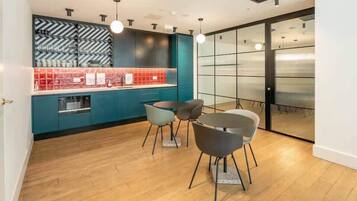 A modern kitchen with teal cabinets, a red backsplash, and a dining area with two chairs.
