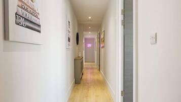 A hallway with framed posters on the walls, a door on the right, and a light fixture on the ceiling.