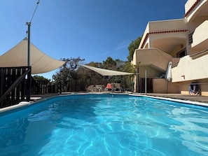 A swimming pool with a wooden deck, a shaded area, and a building with balconies. - 5+1 bedroom family villa with pool and sea view, Vedra and wooded hills (Sant Josep de sa Talaia)