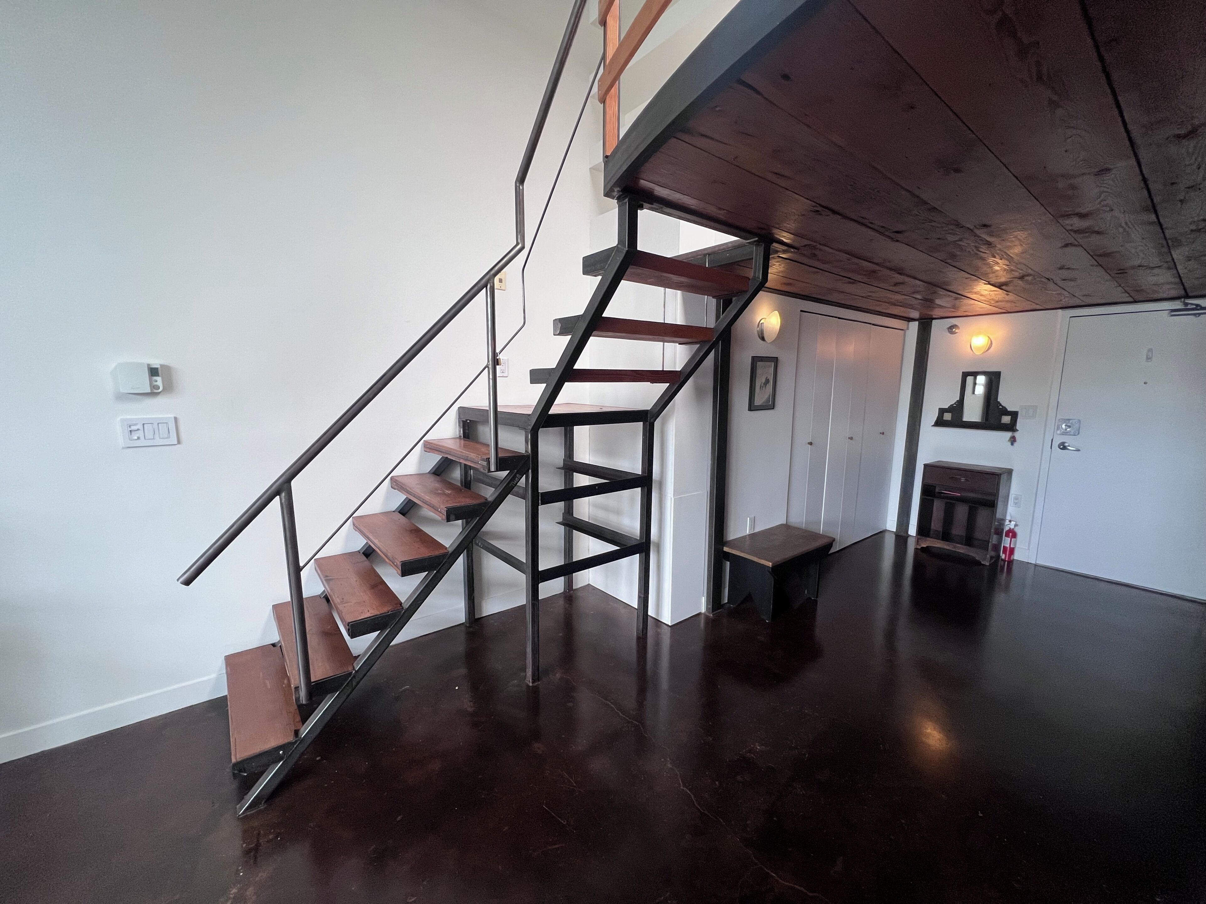 A staircase with wooden steps and metal railings, a white wall with a smoke detector, and a polished dark floor.