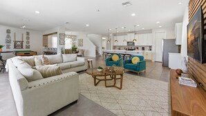 Un salon moderne avec un canapé, une table basse et des fauteuils, une cuisine avec des meubles blancs et un coin repas comprenant une table et des chaises.