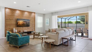 Un salon moderne comprenant un canapé, des fauteuils, une table basse et un téléviseur fixé à un mur en bois.