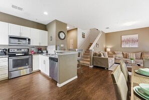 A modern kitchen with stainless steel appliances, a dining area with a wooden table and chairs, and a staircase leading to another level. - Family 4BR Stay Near Orlando Parks (Kissimmee)