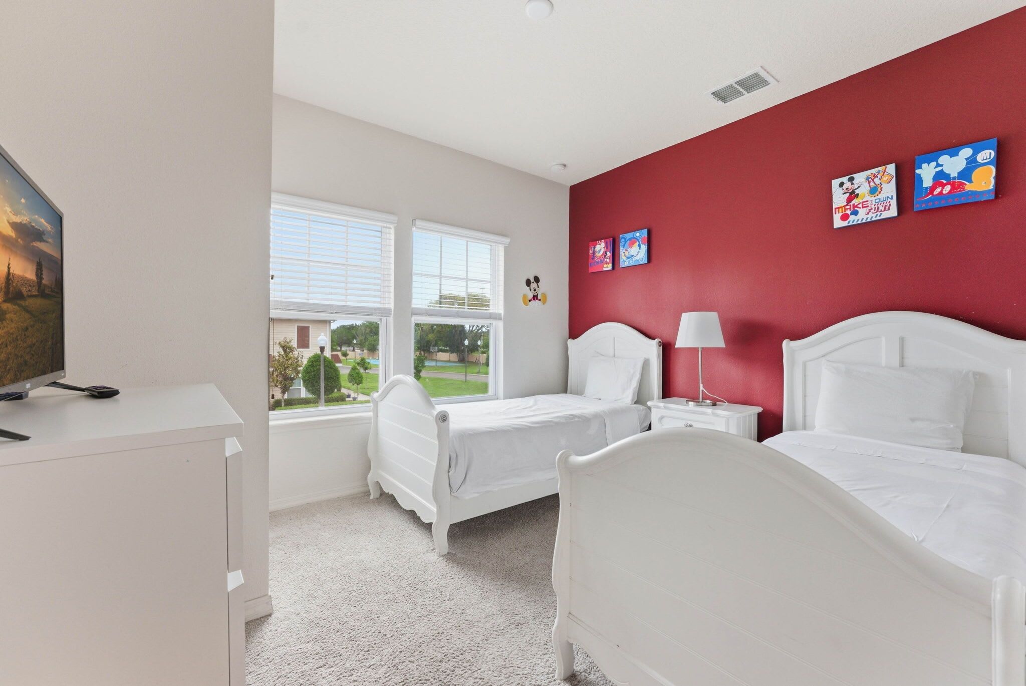 A bedroom with two beds, a desk, a TV, and a window with blinds.