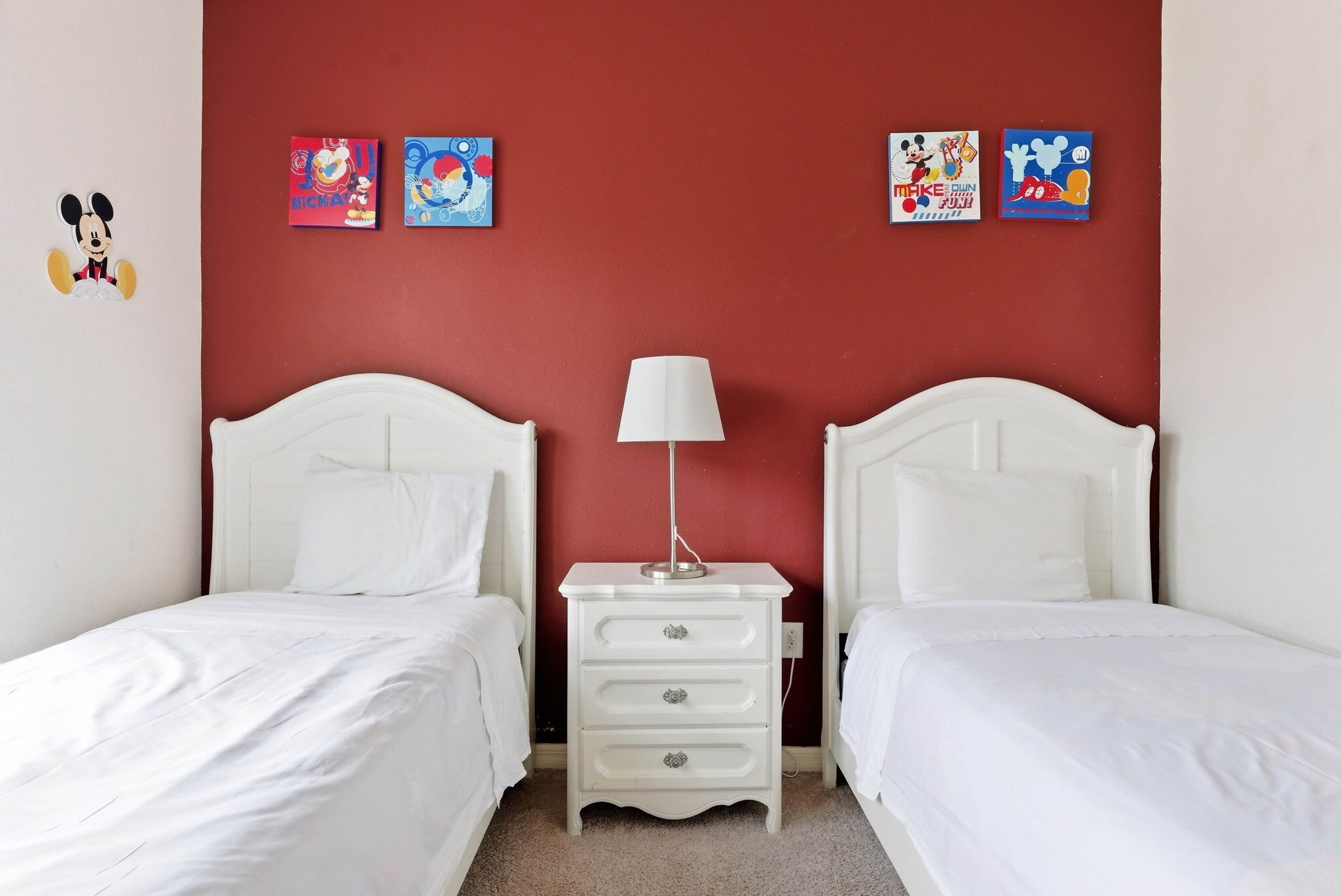Una habitación con dos camas blancas, una mesita de noche blanca con una lámpara y paredes rojas.