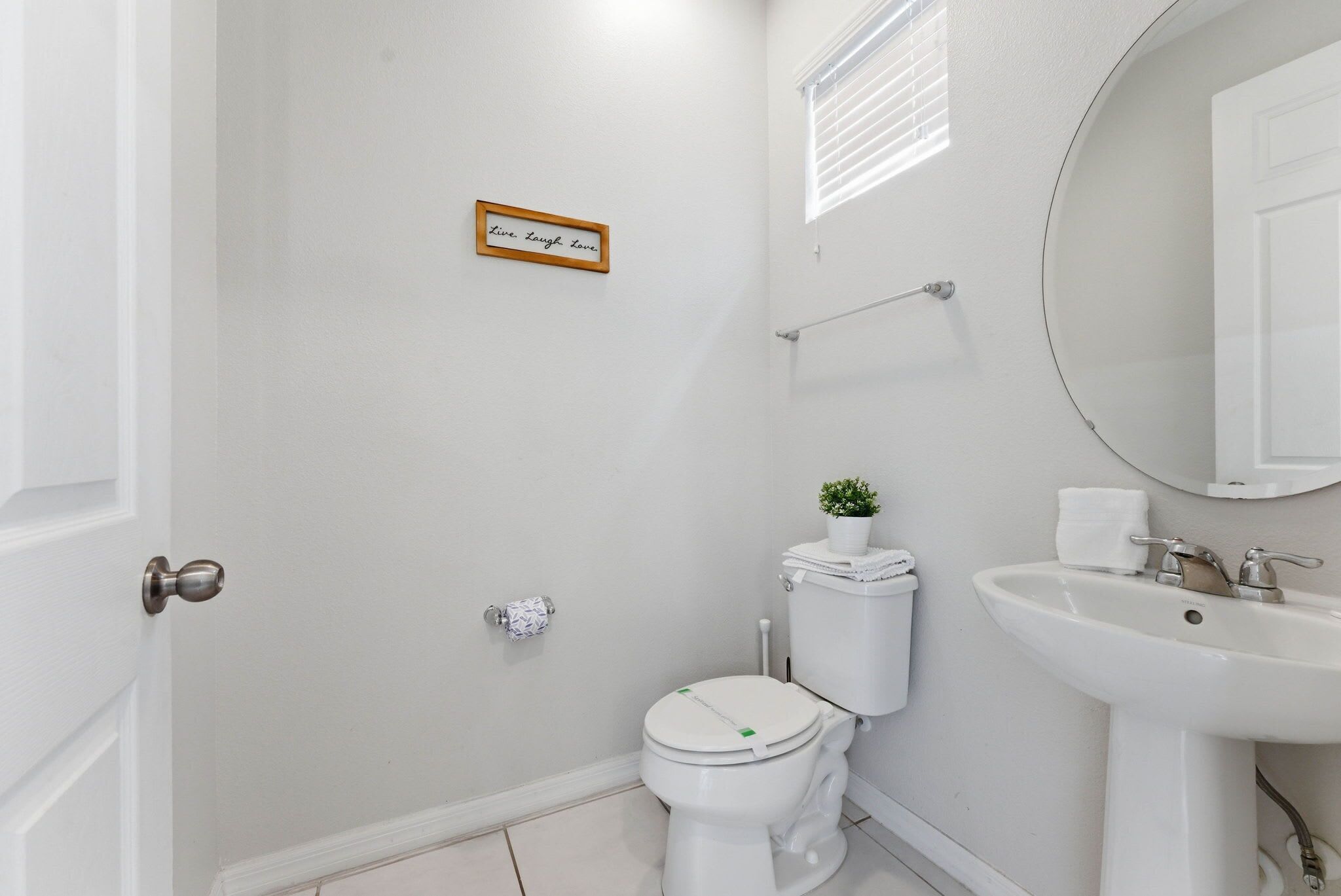 Une salle de bain avec des toilettes, un lavabo et une affiche portant l’inscription « Vivez. Riez. Aimez. »
