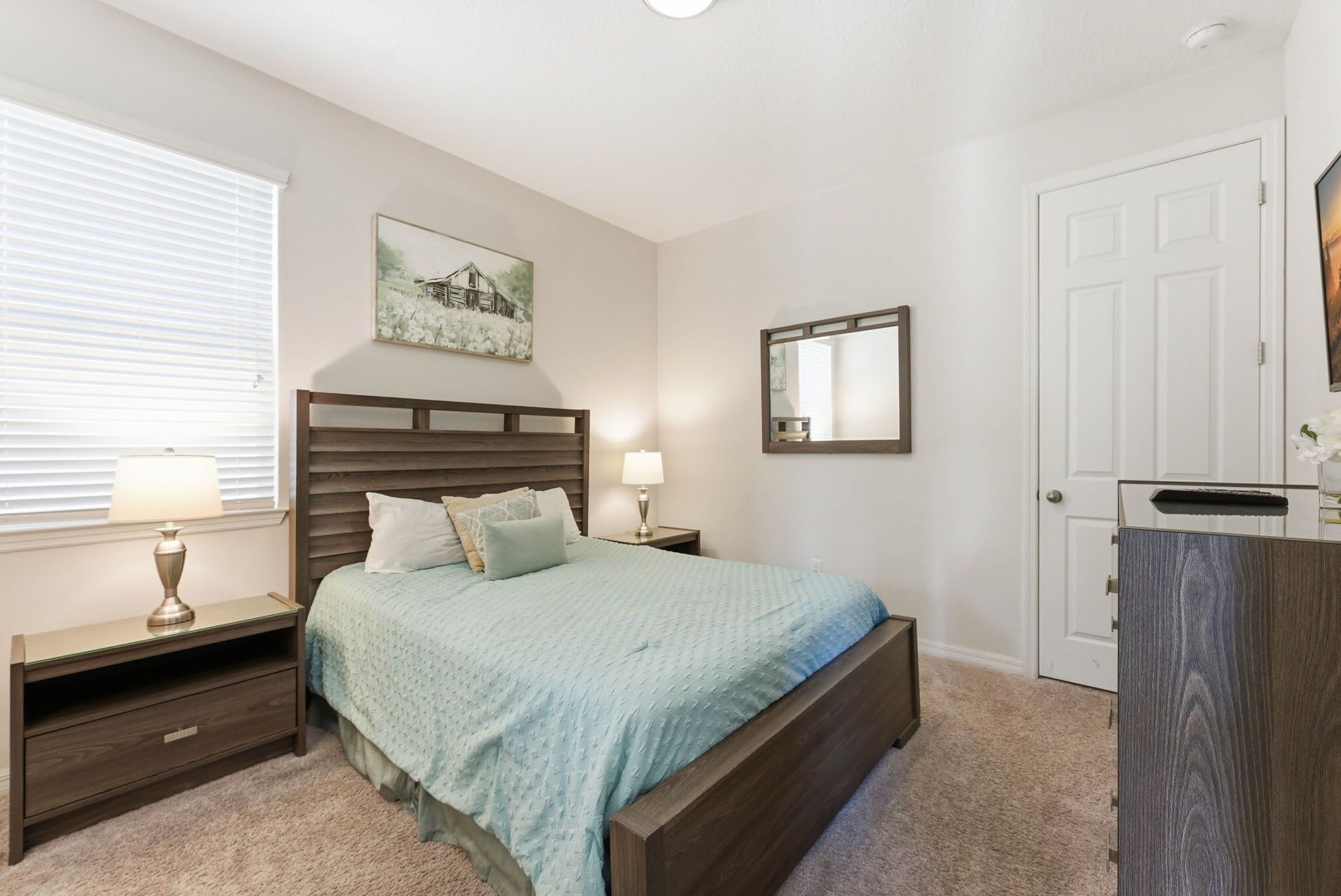 A bedroom with a bed, nightstands, a dresser, a window with blinds, a painting, and a door.