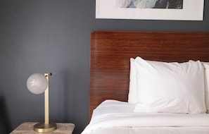 Una cama con ropa de cama blanca, un cabecero de madera y una mesita de noche con una lámpara.