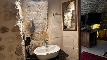 Un baño con pared de piedra, un lavamanos blanco, armarios de madera y un espejo.