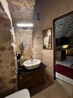 Un baño con pared de piedra, un lavamanos blanco, armarios de madera y un espejo.