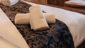 A room with a stone wall, a wooden door, a bed with towels, a chair, and a table with a kettle. - MAROVA BOUTIQUE HOTEL (Artuklu)