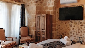 A hotel room with a stone wall, a chandelier, a bed, a TV, a wardrobe, and a chair. - MAROVA BOUTIQUE HOTEL (Artuklu)