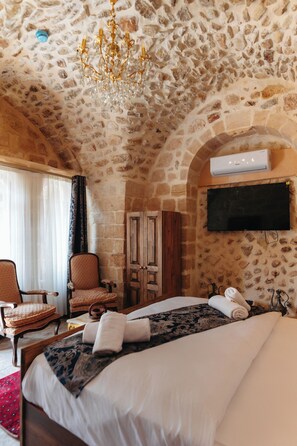 Habitació d'hotel amb paret de pedra, un penjallum, un llit, un televisor, un armari i una cadira.