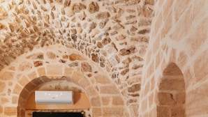 A bedroom with a stone wall, a flat-screen TV mounted above a bed, and a bedside table with a lamp. - MAROVA BOUTIQUE HOTEL (Artuklu)
