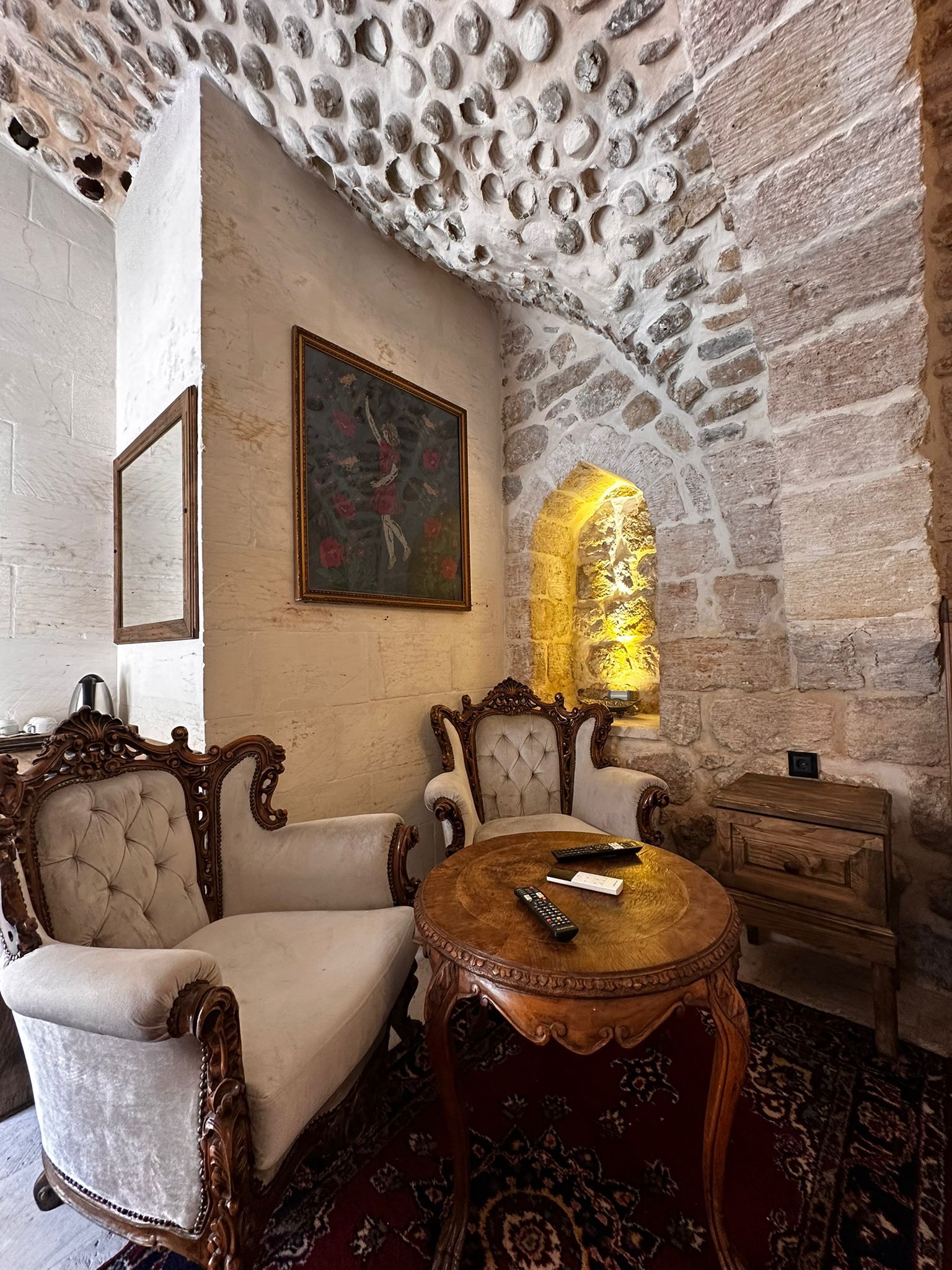 A room with a stone wall, a painting, a sofa, a table, and a wooden cabinet.
