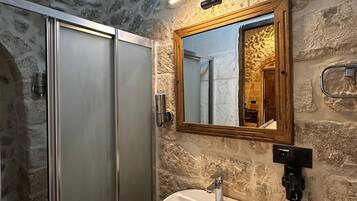 Une salle de bain avec un mur en pierre, un meuble-lavabo en bois, un lavabo blanc et un miroir.