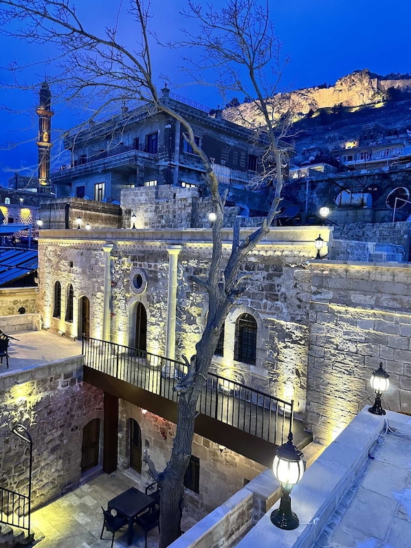 Un edificio de piedra con varios niveles, balcones y un árbol en primer plano.