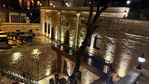 A stone building with arched windows and a balcony overlooking a courtyard with tables and chairs. - MAROVA BOUTIQUE HOTEL (Artuklu)