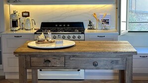 Una cocina con una mesa de madera, dos lámparas colgantes, una estufa y una ventana.