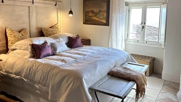 Un dormitorio con una cama grande, techo de madera, ventana con cortinas y un cuadro en la pared.