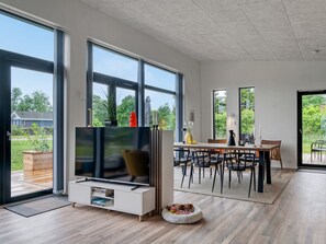 En moderne stue med TV, spiseområde og store vinduer.