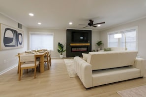 A living room with a sofa, dining table, chairs, a TV, and a ceiling fan.