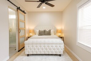 Quarto com cama estofada, duas luminárias de cabeceira, ventoinha no teto e porta de vidro deslizante.