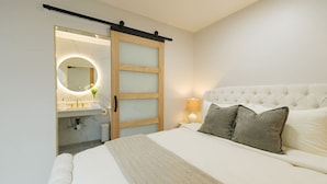 Une chambre à coucher comprenant un lit, une table de chevet, une lampe, une porte coulissante et une salle de bain avec un miroir.