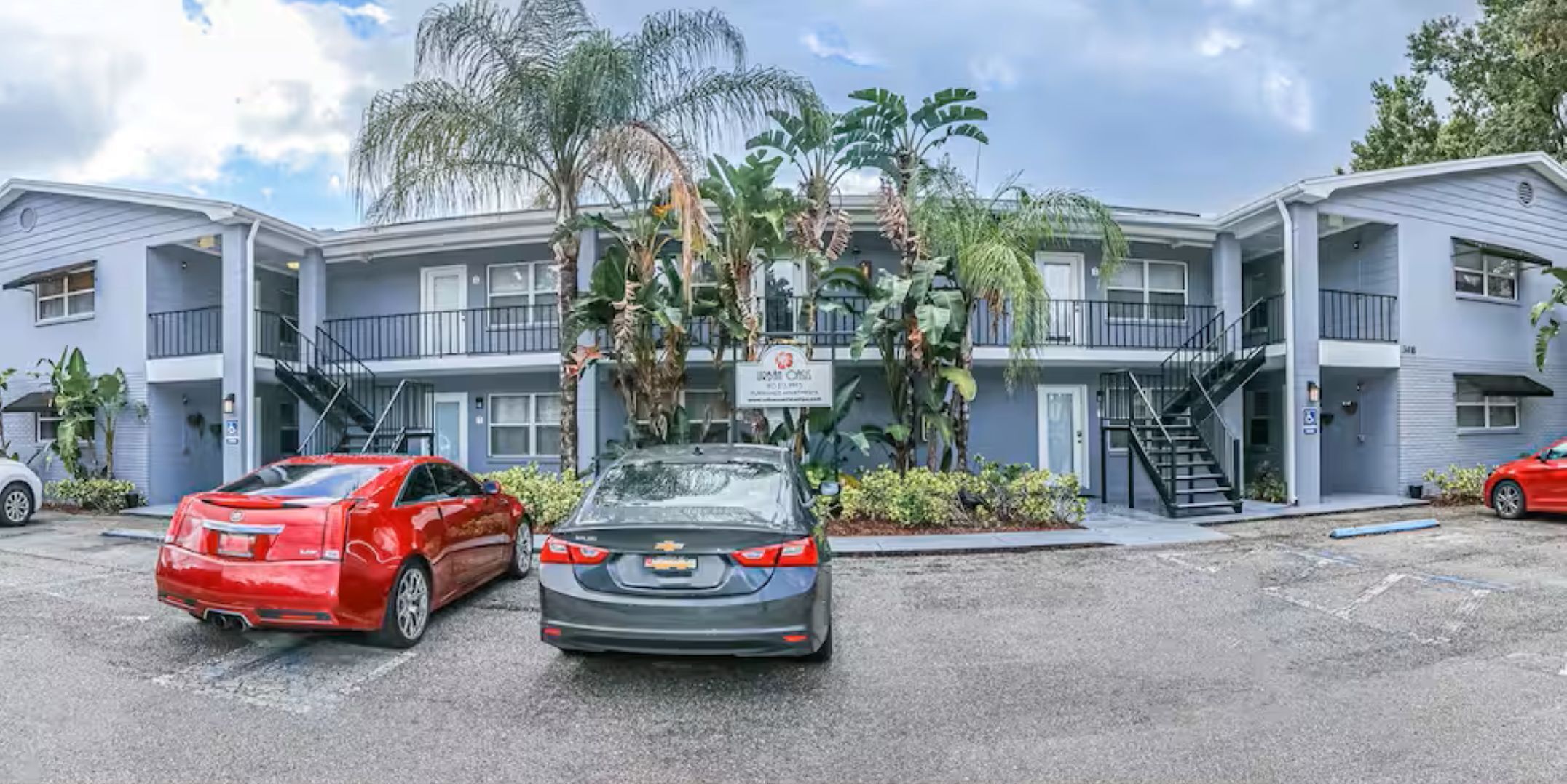 A two-story motel with a parking lot, a red car, and a sign indicating a pet-friendly policy.