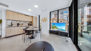 Eine moderne Küche mit Holzausstattung, ein Essbereich mit rundem Tisch und Stühlen, ein großer Flachbildfernseher und ein Balkon mit Blick auf die Stadt.