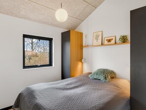 A bedroom with a bed, a window, a shelf with framed pictures, and a hanging light fixture. - "Anttoni" - 350m from the sea by Interhome (Sæby)
