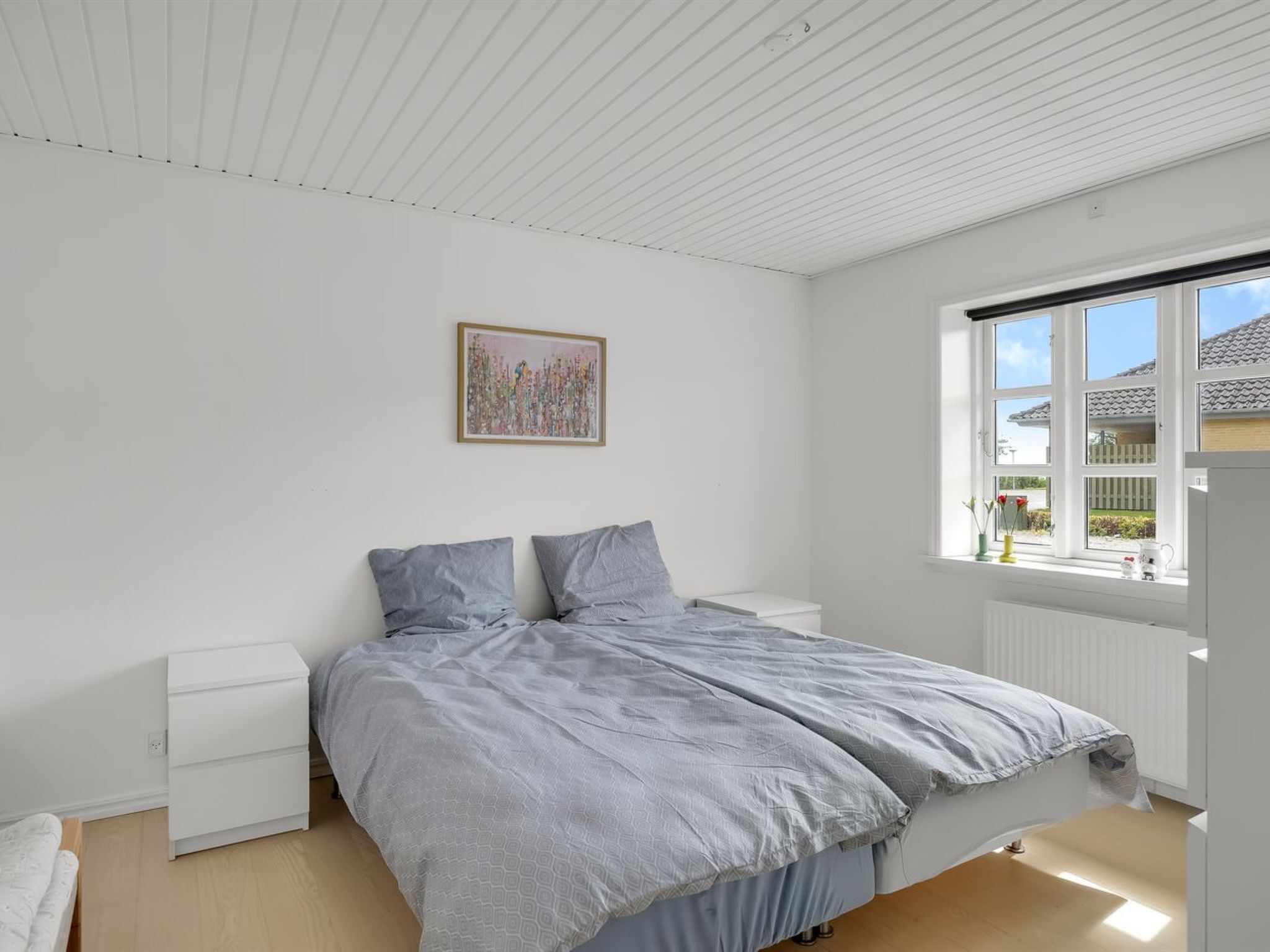 Un dormitorio con cama, mesita de noche, ventana con vistas y un cuadro en la pared.
