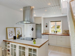 Une cuisine moderne dotée d’un îlot central, de meubles blancs, d’une hotte en acier inoxydable et d’une fenêtre offrant une vue agréable.