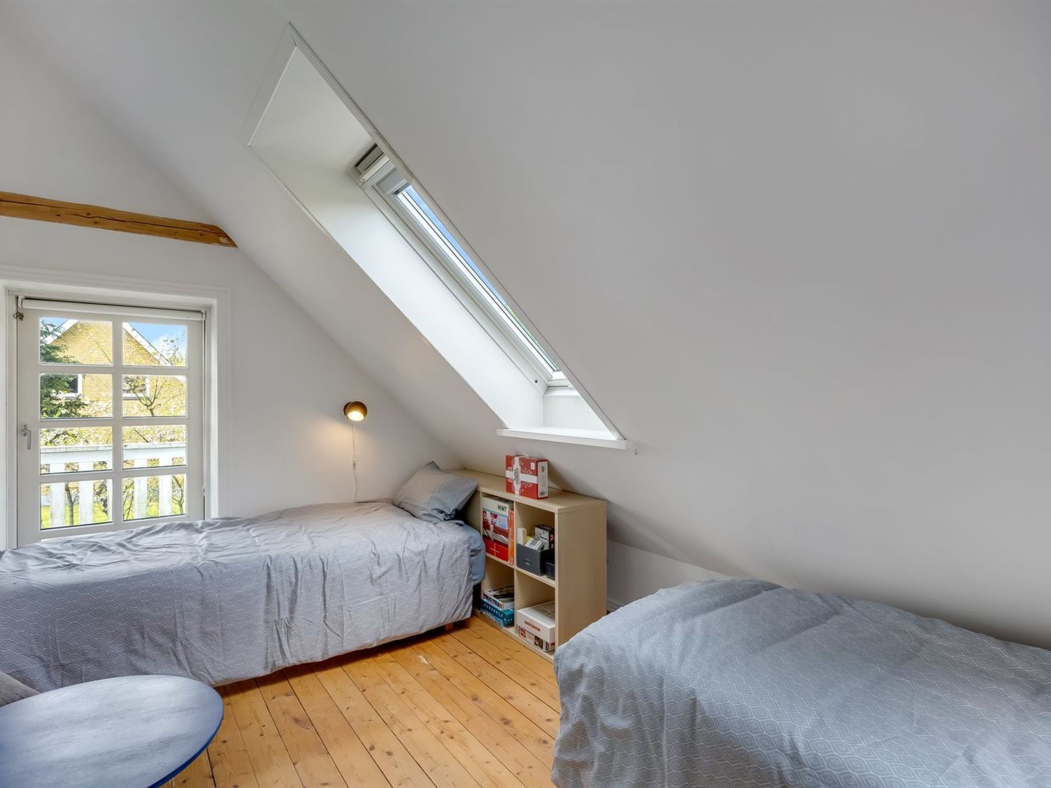 A room with two beds, a skylight, a small table, and a bookshelf.