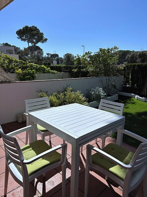 Un patio con mesa y sillas blancas, rodeado de vegetación y un cielo despejado.