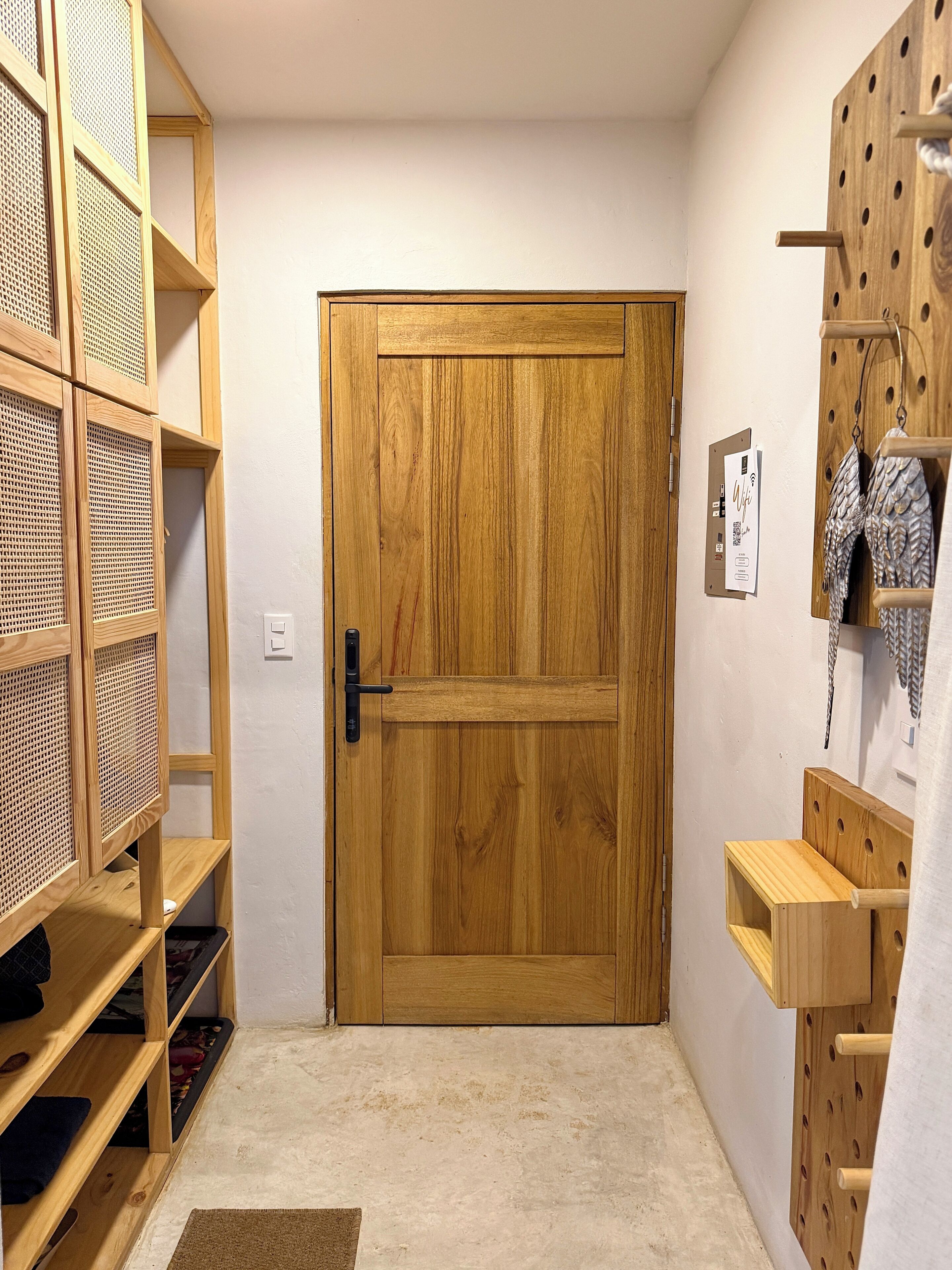 Une porte en bois avec une poignée, une petite étagère sur laquelle se trouve un objet blanc, et un porte-objets fixé au mur.