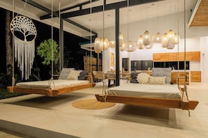 A modern bedroom with a swing bed, a macrame wall hanging, and a dining area with wicker chairs. - Jungle Bungalow near La Fortuna / Peaceful Retreat + Pool / Heliconia (Ciudad Quesada)