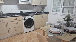 Une cuisine moderne équipée d’un lave-linge, d’une table à manger pour quatre personnes et d’une fenêtre avec des stores.